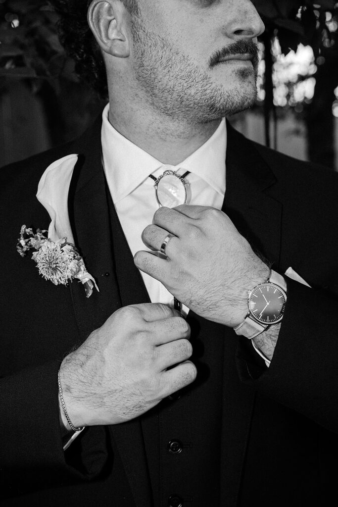 Groom adjusting his tie with soft window light